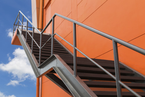 金属防火逃亡或紧急出口在建筑物的橙色墙上，蓝天和白云